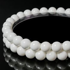 a white beaded bracelet is shown on a black surface, with reflection in the background