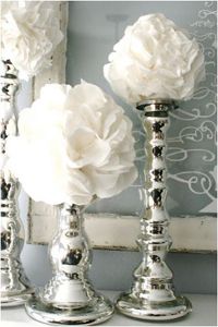 three silver candlesticks with white flowers in them sitting on a shelf next to a mirror