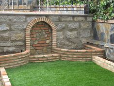 a brick fire place sitting in the middle of a green lawn next to a stone wall