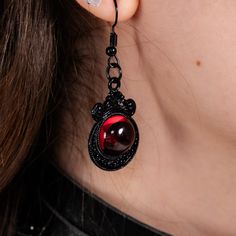 A pair of Gothic earrings adorned with a 1.5 inch tall and 1 inch wide skull made of black painted alloy, accented with a blood red ruby. Gothic Black Drop Earrings, Black Punk Metal Earrings, Black Single Earring For Halloween, Black Gothic Pierced Earrings, Gothic Black Single Earring, Red Punk Earrings For Gifts, Black Vampire Style Jewelry For Party, Edgy Red Jewelry Gift, Edgy Red Jewelry For Gift