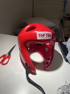 a red plastic helmet sitting on top of a table next to a pair of scissors