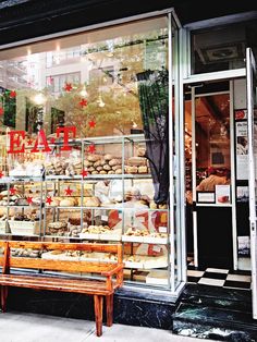 a wooden bench sitting in front of a store window filled with bread and pastries