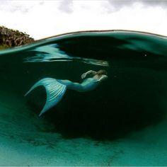 a mermaid is swimming in the ocean with her tail spread out and head above water