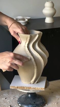 a woman is making a vase out of clay on top of a table with other items