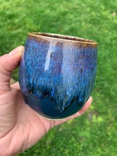 a hand holding a blue cup in front of green grass with trees on the top