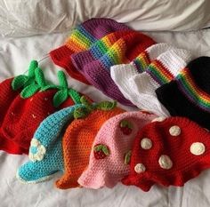 five crocheted hats are lined up on a white sheet, each with different designs and colors