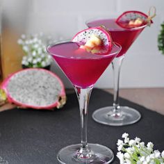 two glasses filled with fruit and garnish sitting on top of a black table