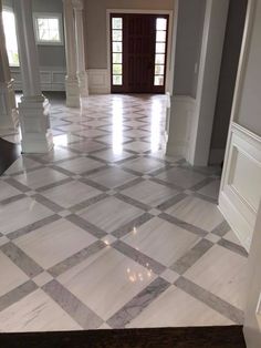 an empty room with marble flooring and white pillars in the center is seen from the doorway