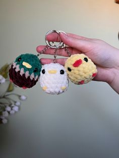 hand holding three small crocheted keychains in front of a white wall