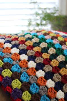 a multicolored crocheted blanket sitting on top of a wooden table next to a potted plant