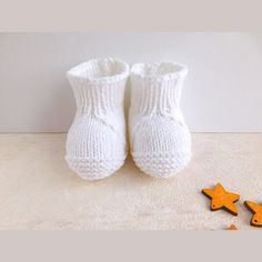 a pair of white knitted baby booties next to star shaped buttons