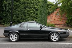 a black sports car parked in a parking space next to a brick wall and trees