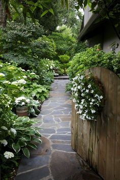 a stone path is lined with white flowers and greenery on either side of the house