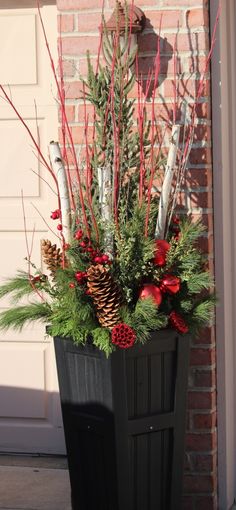 a planter filled with evergreen, pine cones and red berries on the side of a building