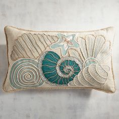 an embroidered pillow with seashells and starfish on the front, against a white wall