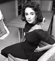 black and white photograph of a woman sitting at a table in a room with wooden furniture