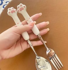 a person holding two forks and spoons with paw prints on them, next to a brown table