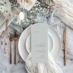 an elegant table setting with white flowers and gold cutlery on the plate, along with silverware