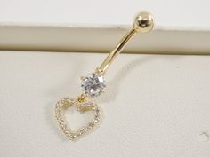 a gold heart shaped belly ring with crystal stones in the shape of a heart, on a white surface