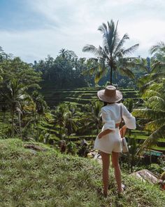 a woman standing on top of a lush green hillside with palm trees in the background