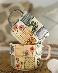 two coffee mugs are stacked on top of each other, one is decorated with flowers and stripes