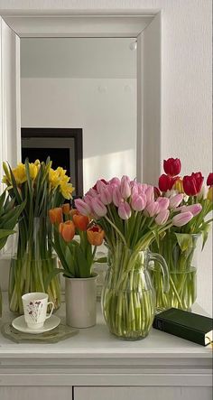 several vases filled with colorful flowers sitting on top of a white table next to a mirror