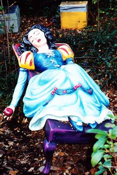 a statue of a woman laying on top of a purple bench in the woods next to some trees