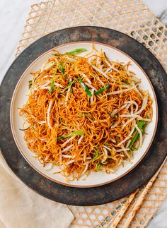 a white plate topped with shredded carrots and green onions next to chopsticks