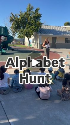 children sitting on the ground in front of a playground with an adult standing at the top