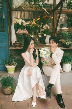 a man and woman sitting next to each other in front of flower shop with potted plants