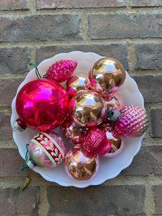 a white plate topped with lots of shiny christmas ornament ornaments on top of a brick wall