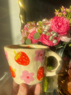 a hand holding a coffee cup with flowers in the background and a mirror behind it