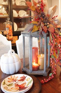 a table topped with plates and candles next to a lantern filled with autumn leaves on top of a wooden table