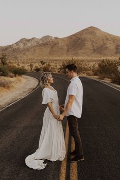 a couple holding hands while standing in the middle of an empty road