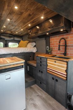 a kitchen and living area in an rv with brick walls, wood flooring and ceiling lighting