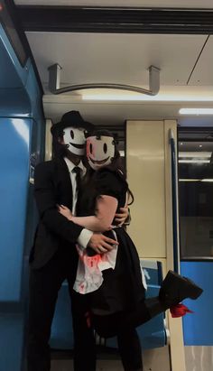 two people dressed in costumes hugging each other on a subway car with their faces painted to look like they are wearing masks