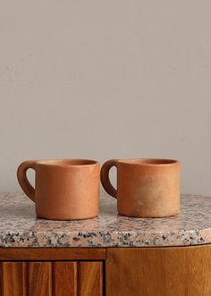 two clay mugs sitting on top of a wooden cabinet