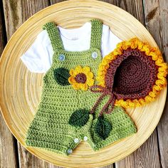 a crocheted sunflower hat and green overalls on a plate