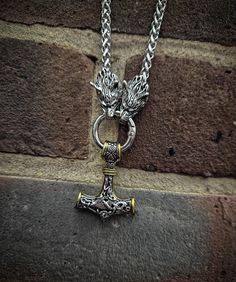 a silver necklace with an anchor and dragon head on it's end, sitting against a brick wall