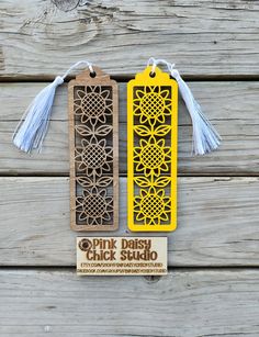 two bookmarks with tassels on them sitting next to each other, one has a tag that says pink daisy chick studio