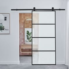 an open sliding door in a white room with a mirror and plant on the wall