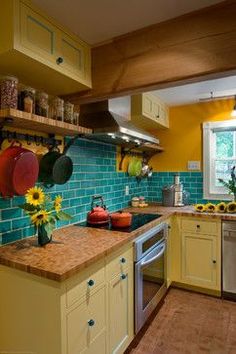 a kitchen with yellow cabinets and green tile backsplash, sunflowers on the counter