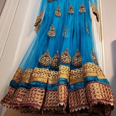 This Is An Amazing Blue Anarkali Dress With Matching Pants And Scarf. The Fabric Has Shining Gold Accents. This Will Make A Great Choice For Any Occasion. Blue Festive Anarkali Set With Traditional Drape, Festive Blue Anarkali Set With Traditional Drape, Blue Anarkali Set For Festive Occasions, Blue Anarkali Set With Sheer Dupatta For Navratri, Festive Blue Anarkali Set, Blue Bollywood Anarkali Set For Designer Wear, Blue Choli With Sheer Dupatta For Navratri, Blue Anarkali Set For Diwali, Blue Bollywood Anarkali Set For Festive Occasions