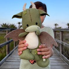 a person holding a stuffed animal in their hands on a wooden bridge near grass and palm trees