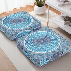 two blue and white pillows sitting on top of a wooden floor next to a table