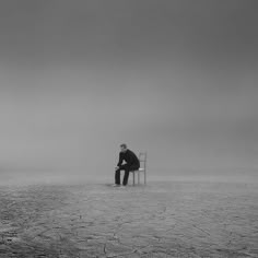 a man sitting on a chair in the middle of a barren area with no one around him