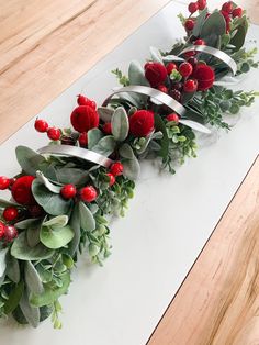 some red flowers and greenery on a white counter top with silver ribbon around them