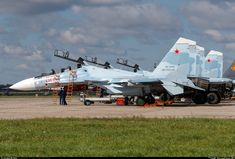 several fighter jets are parked on the tarmac at an airport with men standing around them