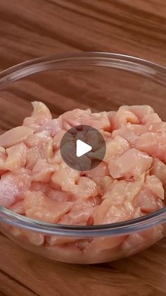 a glass bowl filled with raw chicken on top of a wooden table