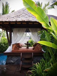 a gazebo sitting next to a pool surrounded by lush green plants and trees on the other side